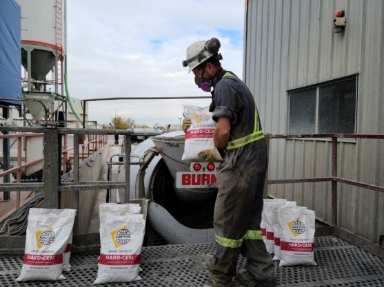 A construction worker is surrounded by Hard-Cem bags and is holding one while preparing to add it to the concrete mix during batching.